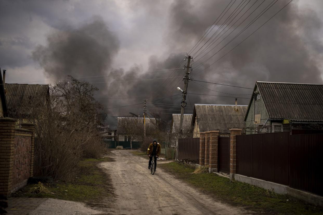 A Ukrainian man rides his bicycle near to a factory and a store burning after being bombarded in Irpin, on the outskirts of Kyiv, Ukraine, Sunday, March 6, 2022.
