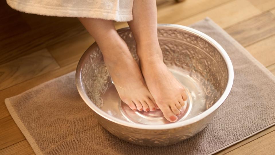 A woman soaking her feet in a bowl of cold water to help remove an ingrown toenail herself