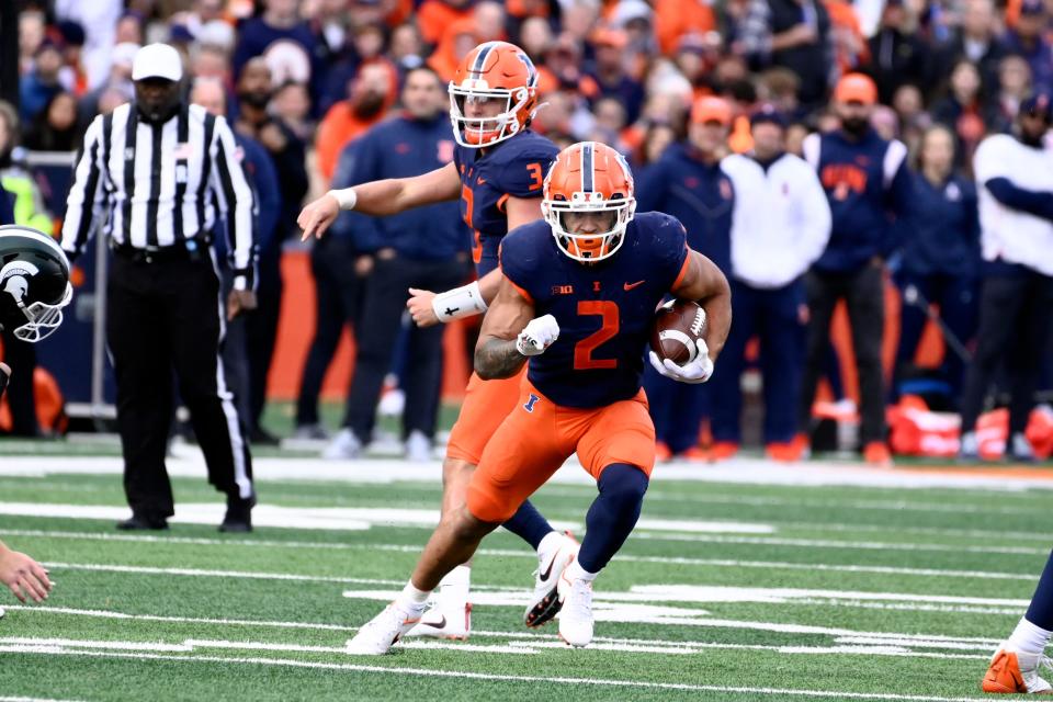 Illinois running back Chase Brown (2) runs with the ball as Illinois quarterback Tommy DeVito (3) looks on during the first half of an NCAA college football game against Michigan State, Saturday, Nov. 5, 2022, in Champaign, Ill. (AP Photo/Matt Marton)