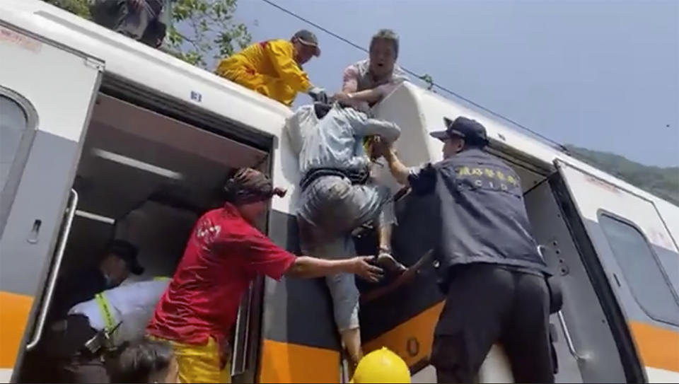 En esta imagen tomada de un video publicado por hsnews.com.tw, un pasajero (centro) recibe ayuda para subir encima de un tren descarrilado en la región de Hualien, en el este de Taiwán, el 2 de abril de 2021. (hsnews.com.tw vía AP)