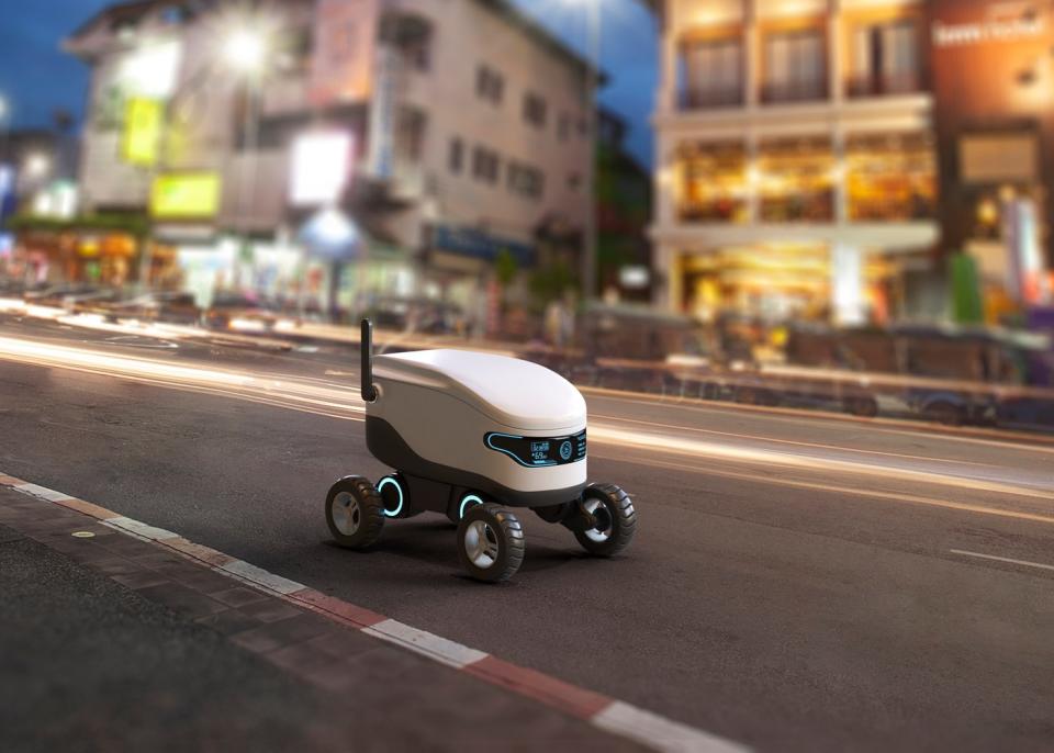 An autonomous delivery robot driving along the road at dusk.