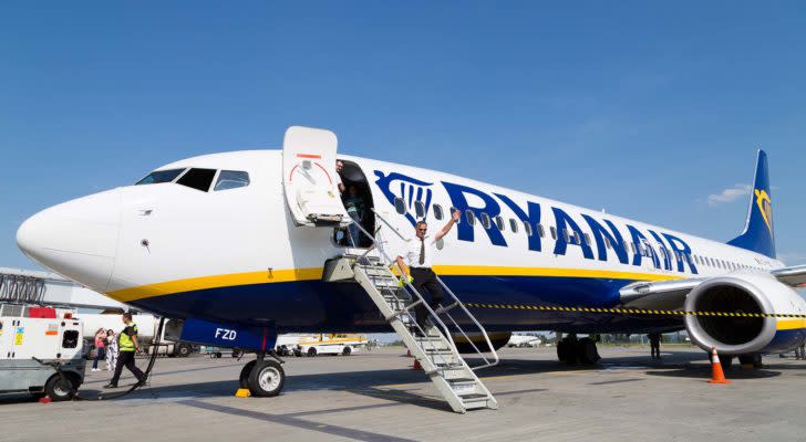 An image of a pilot walking out of a large white, blue, and yellow Ryanair plane.