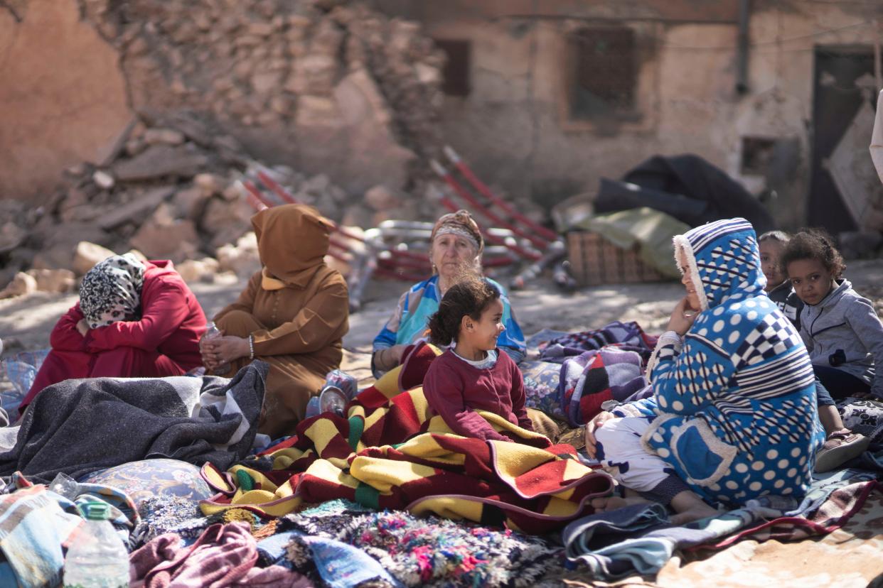 Families sit outside their destroyed homes near Marrakech (AP)