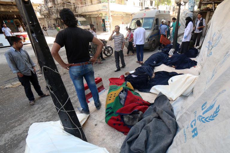 Civilians stand next to the bodies of those killed in a reported bomb barrel attack by the Syrian airforce on the eastern Shaar neighbourhood of the northern Syrian city of Aleppo on May 30, 2015