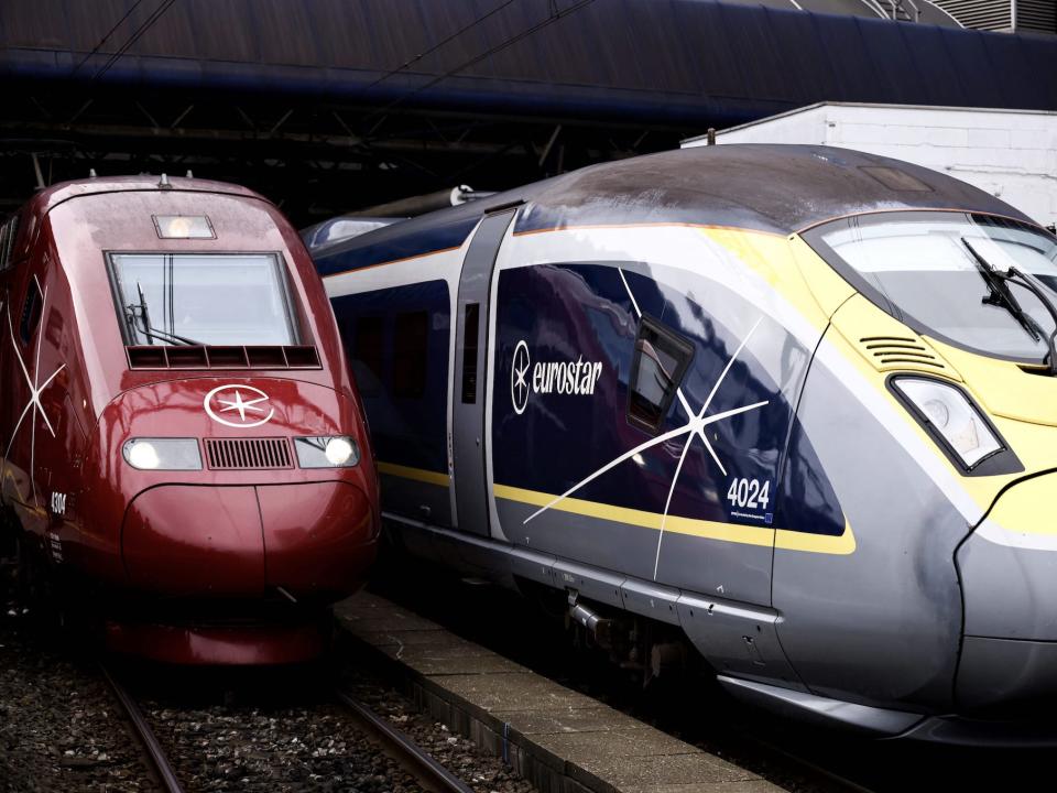 A red Thalys and a yellow and grey Eurostar train side-by-side with the new company logo at Brussels station.