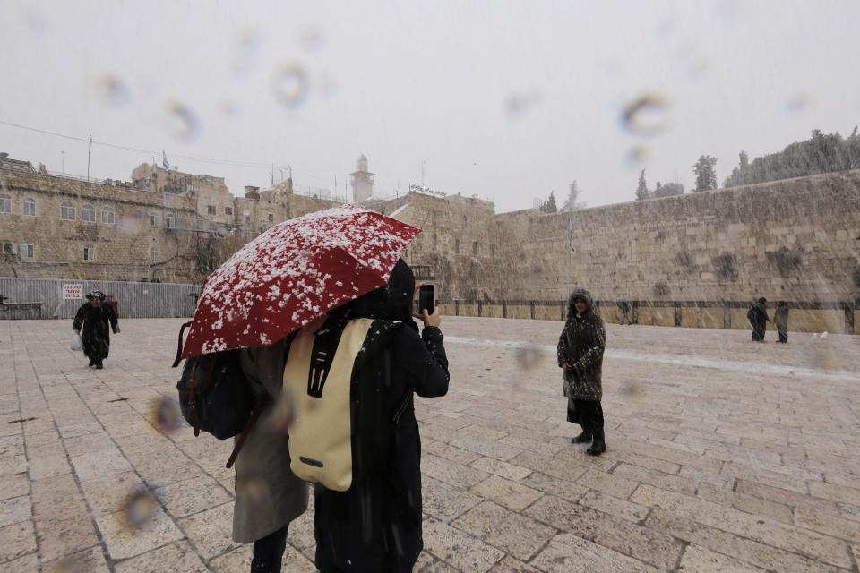 A woman has her picture taken as snow falls near the Western Wall in Jerusalem's Old City December 12, 2013. REUTERS/Ammar Awad (JERUSALEM - Tags: RELIGION ENVIRONMENT)