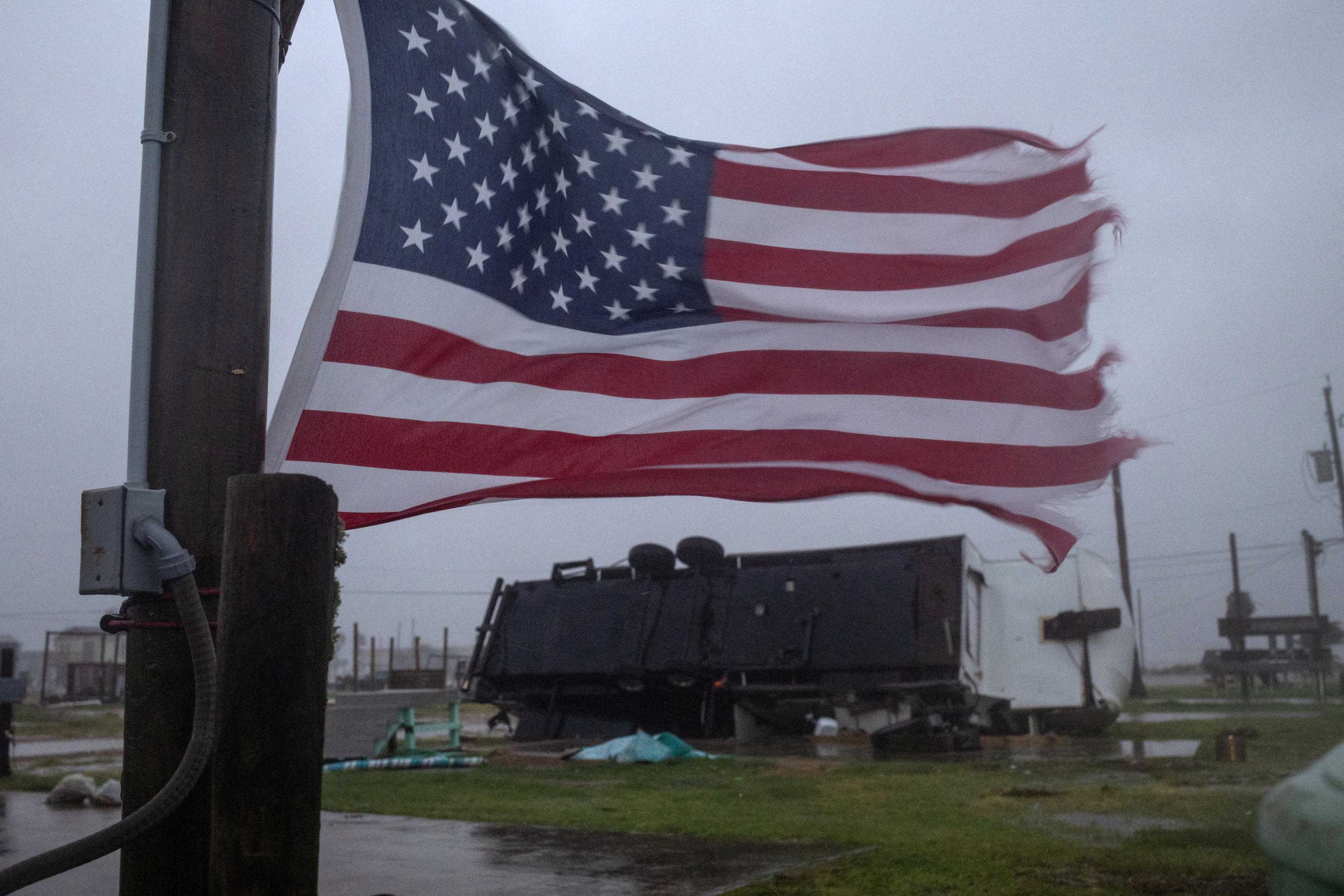 A tattered U.S. flag waves near a trailer home left overturned by Hurricane Beryl winds in Surfside Beach, Texas.