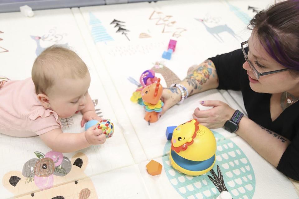 A volunteer at Endeavor Elementary's onsite daycare plays with an infant, whose mom teaches second grade at the school, on Feb. 29, 2024, in Nampa, Idaho. (Darren Svan/Idaho Education News via AP)