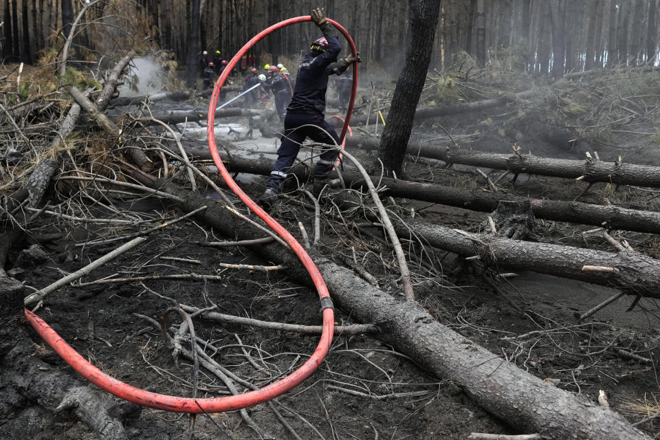 A firefighter unrolls a hose to spray water to put out the remains of fires in a forest in Hostens, south of Bordeaux, southwestern France, Tuesday, Aug. 23, 2022. The season of heat waves and wildfires produced excellent grapes, despite lower yields. (AP Photo/Francois Mori)