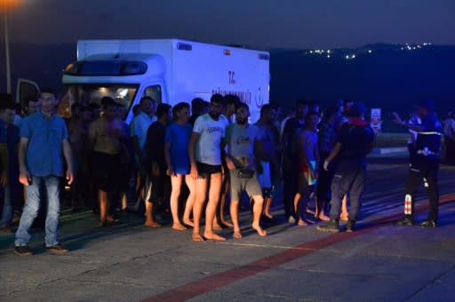 Refugess stand next to an ambulance car as they wait at Tasucu port in Mersin, south-central Turkey, on July 18, 2018 after a boat carrying migrants sank in the Mediterranean Sea off the north of Cyprus