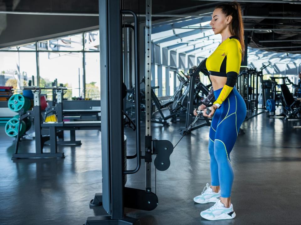 a woman in athletic clothes doing a cable curl exercise on a gym machine, working out the biceps arm muscles