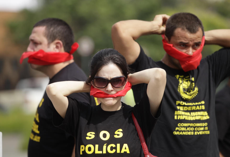 Federal police wearing T-shirts that read in Portuguese "SOS Federal Police" cover their mouths with bandanas as a way to protest their leaders' recommendation to not protest, as they demand better labor conditions outside the venue where Brazil's coach is announcing his squad for the upcoming World Cup in Rio de Janeiro, Brazil, Wednesday, May 7, 2014. Federal police are threatening to go on strike during the international soccer tournament if their demands are not met. (AP Photo/Silvia Izquierdo)