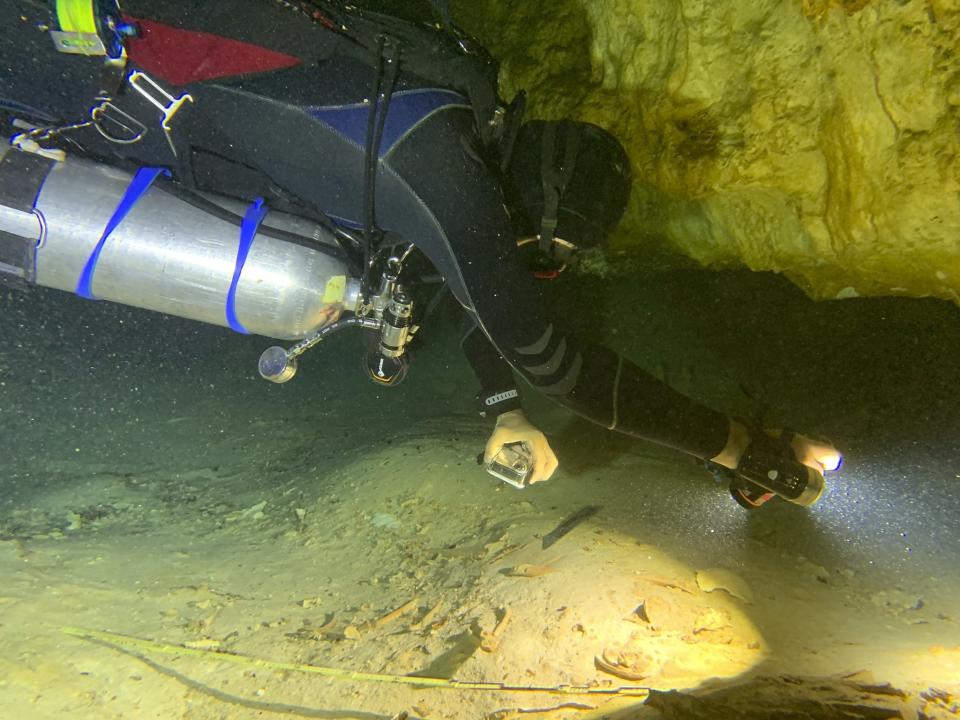 In this photo courtesy of Peter Broger, aquatic archaeologist Octavio del Rio films a pre-historic human skeleton partly covered by sediment in an underwater cave in Tulum, Mexico, Sept. 10, 2022. The cave system was flooded at the end of the last ice age 8,000 years ago, according to an archaeologist and cave diver Octavio del Rio, and is located near where the government plans to build a high-speed tourist train through the jungle. (Peter Broger via AP)