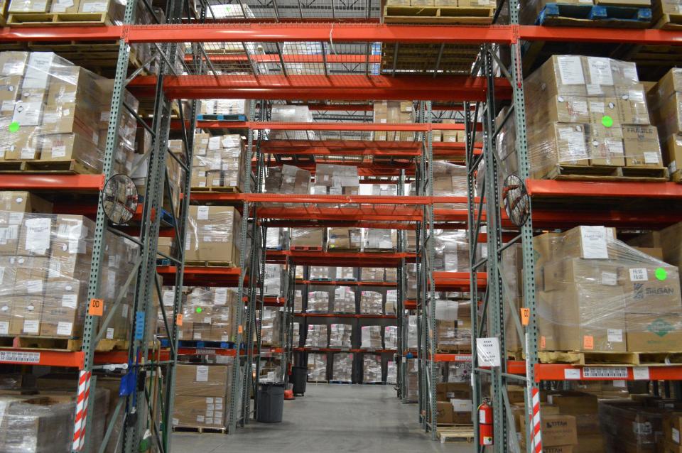 Many rows of cardboard boxes sit on orange shelves inside a large warehouse.