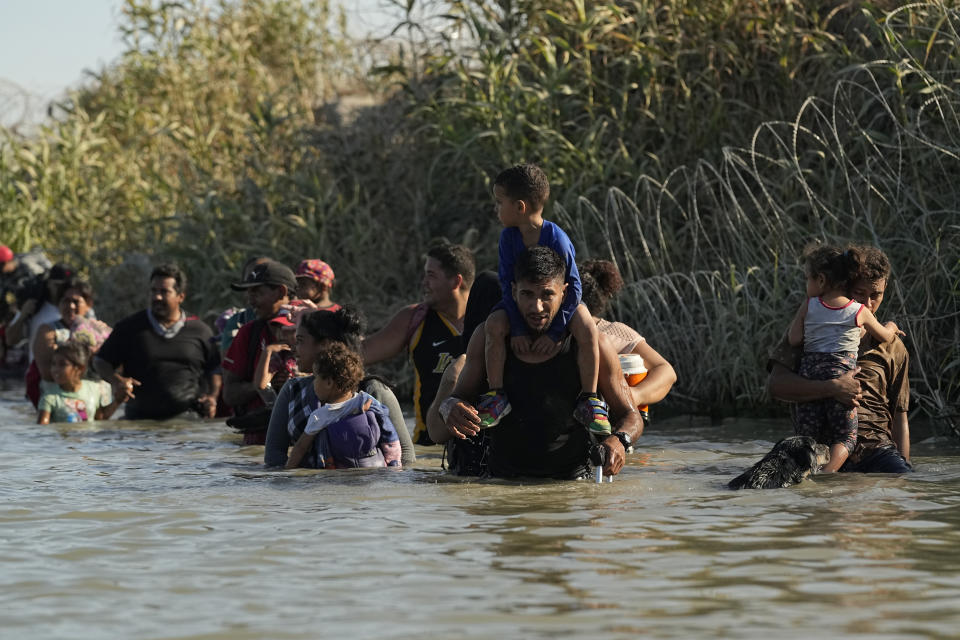 Migrants waist-deep in water, carrying children on their shoulders.