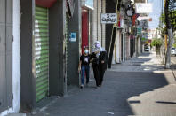 Palestinians wearing face masks walk next to closed shops in Gaza City, Thursday, Aug. 27, 2020. On Wednesday Gaza's Hamas rulers extended a full lockdown in the Palestinian enclave for three more days as coronavirus cases climbed after the detection this week of the first community transmissions of the virus in the densely populated, blockaded territory. (AP Photo/Khalil Hamra)