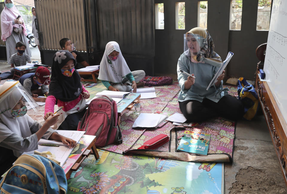 Teacher Inggit Andini, right, wearing a face shield as a precaution against the coronavirus outbreak, speaks as her students in a makeshift classroom at her residence in Tangerang, Indonesia, Monday, Aug. 10, 2020. Andini offered free extra lessons for students who lack access to the internet as the school where she works at remain closed and switched to online learning due to the outbreak. (AP Photo/Tatan Syuflana)