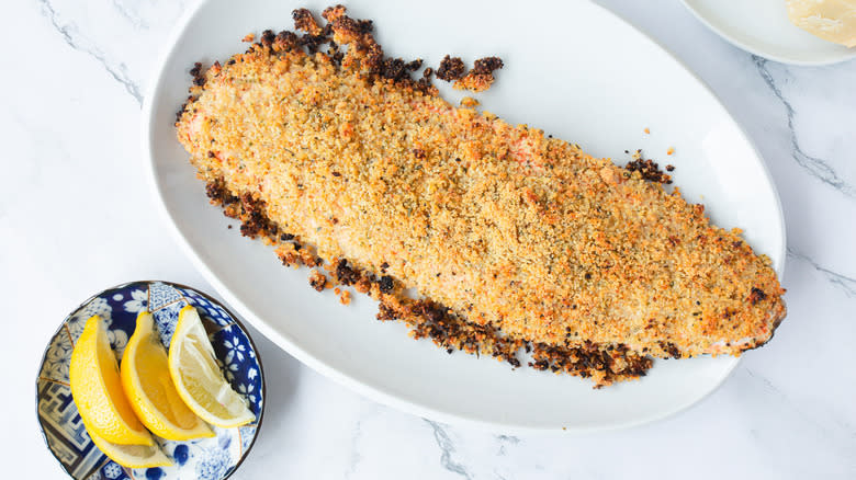 breadcrumb crusted salmon on white platter with lemons