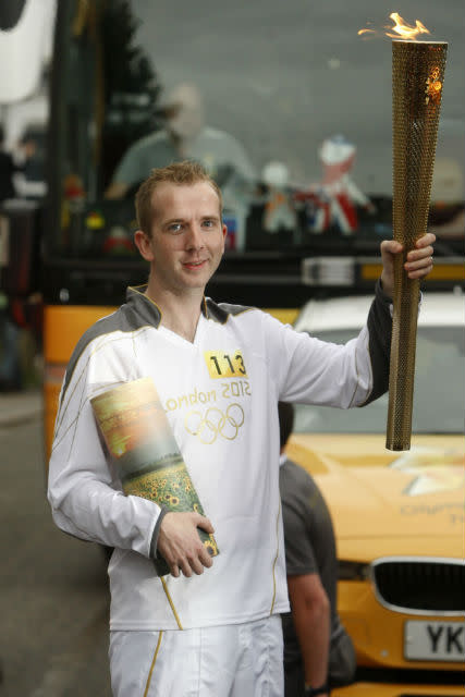 Mark Reynolds holds the ashes of his brother and originally nominated Torchbearer, David, as he carries the Olympic Flame on the Torch Relay leg between Newmarket and Cambridge.