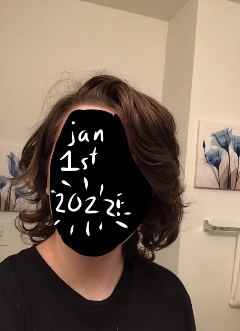 Person with shoulder-length wavy hair in a room, text on face covering features reads "Jan 1st 2022"