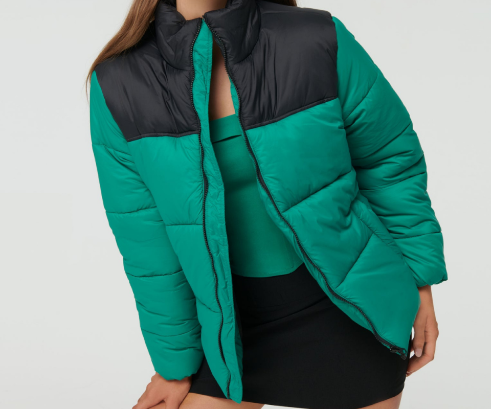 A caucasian woman wears a green and black two-tone puffer jacket against a white background.