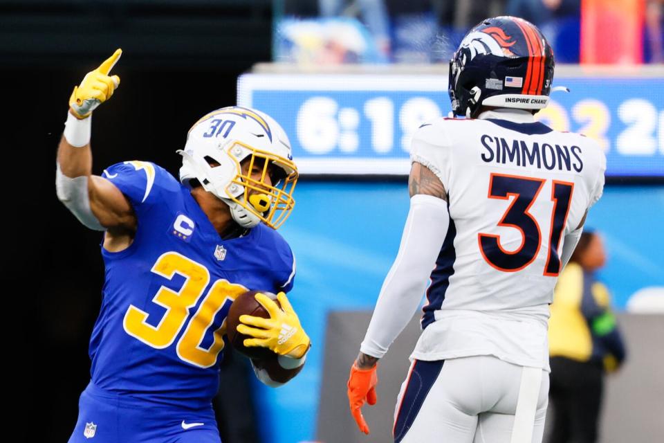 Chargers running back Austin Ekeler (30) reacts after getting a first down as Broncos safety Justin Simmons watches.