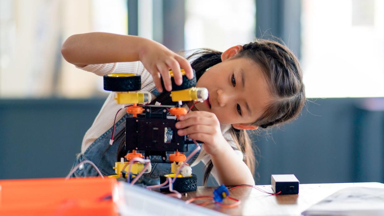 young girl adding wheel to robot