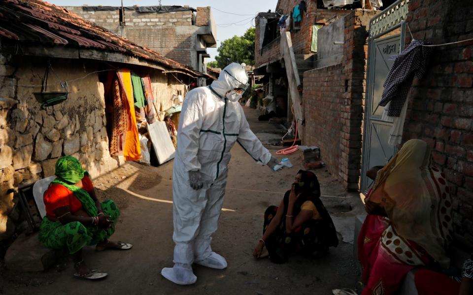 A healthcare checks the temperature of a woman sitting outside her house in an alley during a door-to-door survey for the coronavirus in Jakhan village in the western state of Gujarat - Reuters