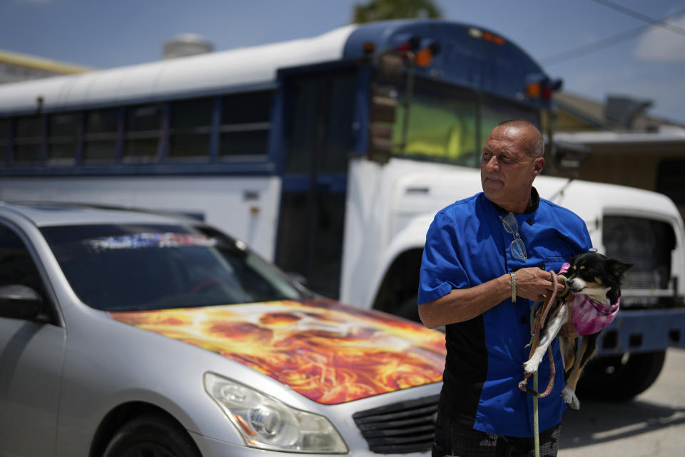 Chef Michael Cellura holds his 15-year-old dog Ginger as he stands beside the car the pair have been living out of for months, after Cellura lost his camper in Hurricane Ian, in Fort Myers Beach, Fla., Thursday, May 11, 2023. There's a lot of us like me that are displaced. Nowhere to go," said Cellura, 58, who sleeps in a parking lot along with other survivors living in RVs and a converted school bus. Cellura, whose waterfront workplace never reopened and who only found work as a chef again in April, has done odd jobs detailing and customizing cars to afford his $500/month car payments and enough gas to keep Ginger safely air conditioned while he works. (AP Photo/Rebecca Blackwell)