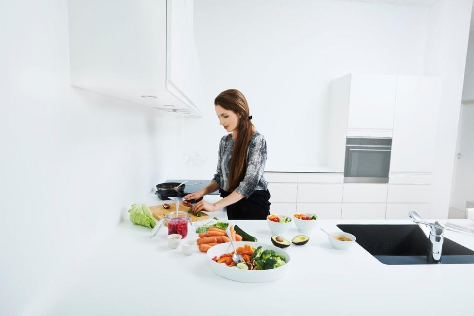 Woman preparing colorful vegetables in an almost all-white kitchen with a black sink.