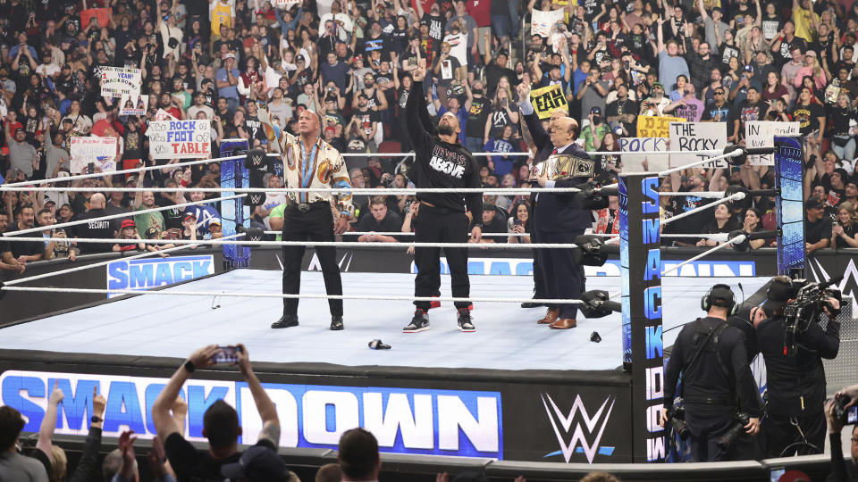 This undated photo provided by the WWE shows from left, Dwayne "The Rock" Johnson, Roman Reigns and Paul Heyman in the ring during WWE Smackdown. As WWE gears up for its biggest annual premium live event in April 2024, the company continues to harness the power of its social media presence to reach its fans. A key component of that strategy is YouTube, where WWE has hit an important milestone: reaching 100 million subscribers. (Scott Brinegar/WWE via AP)