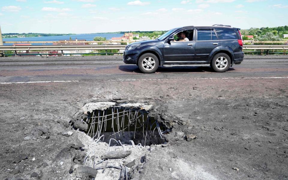 A car moving past a crater on Kherson's Antonovsky bridge - AFP