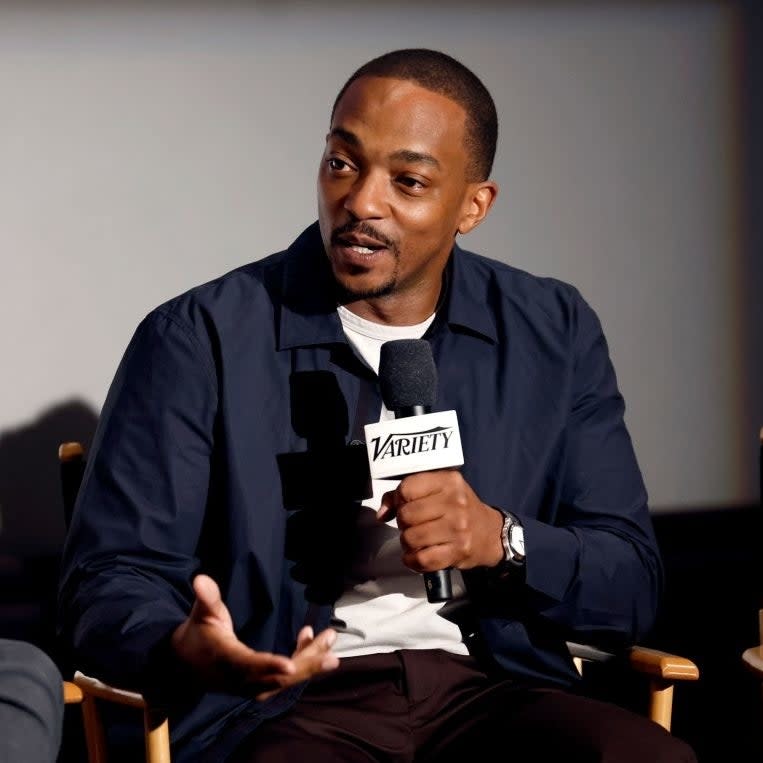 Anthony Mackie speaks into a Variety microphone while seated, wearing a casual jacket over a white shirt, in an interview setting