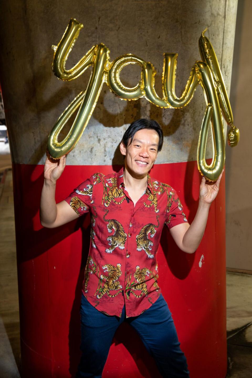 Man with red shirt holding balloon spelling the word "Yay"