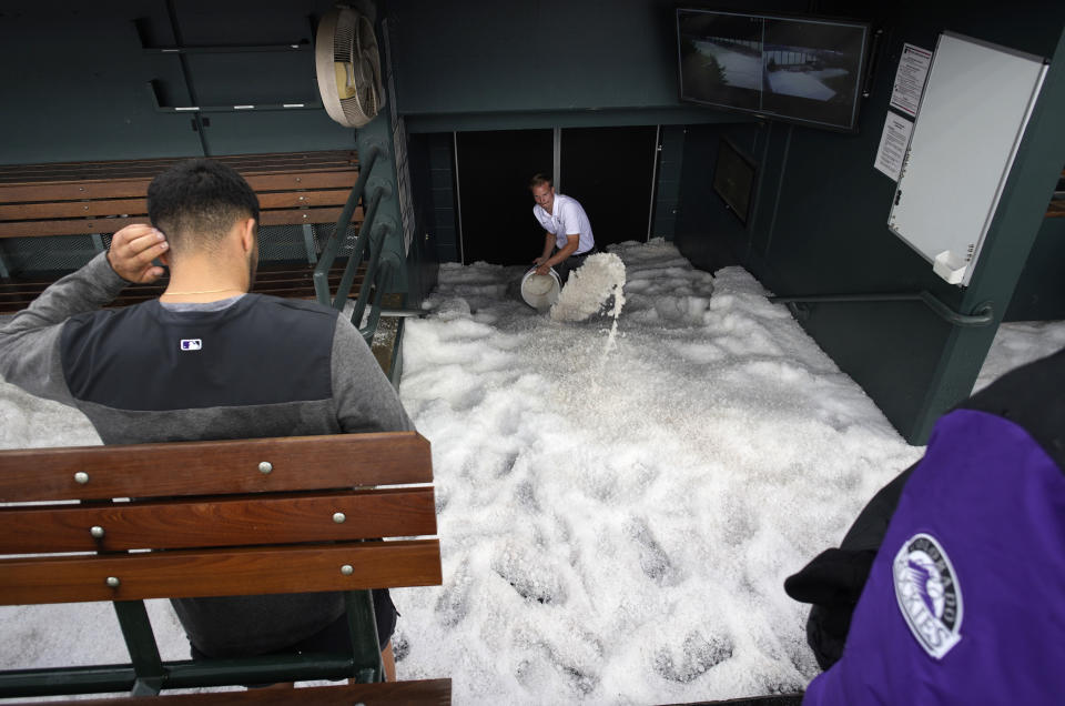Clubhouse attendant Casey Williams, back right, uses a bucket to clear a mixture of water and hail from in front of the home dugout doors to the clubhouse after a summer storm packing heavy rain, high winds and large hail swept over Coors Field, Thursday, June 29, 2023, in Denver. The Colorado Rockies were set to host the Los Angeles Dodgers, Thursday. (AP Photo/David Zalubowski)