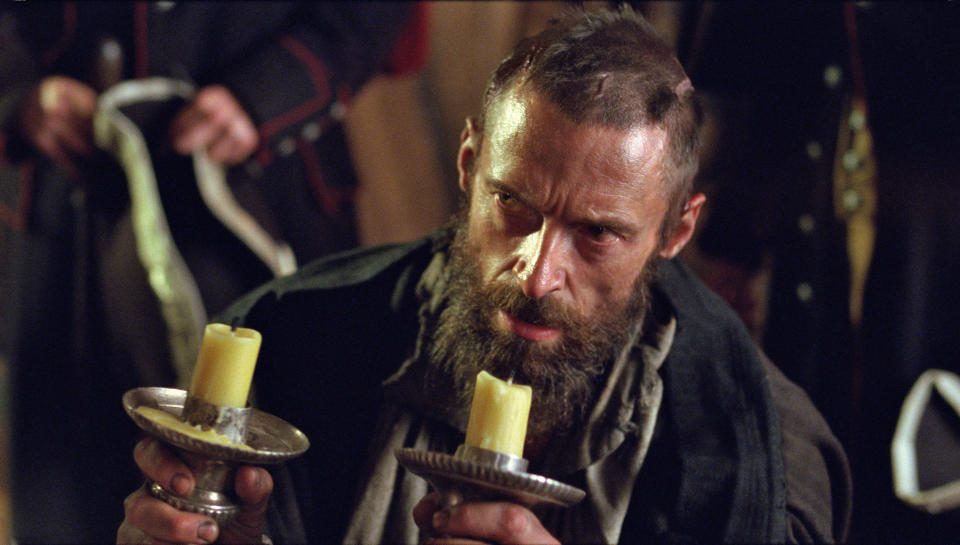 high jackman with a shaved head holding candlesticks as jean valjean in les misérables