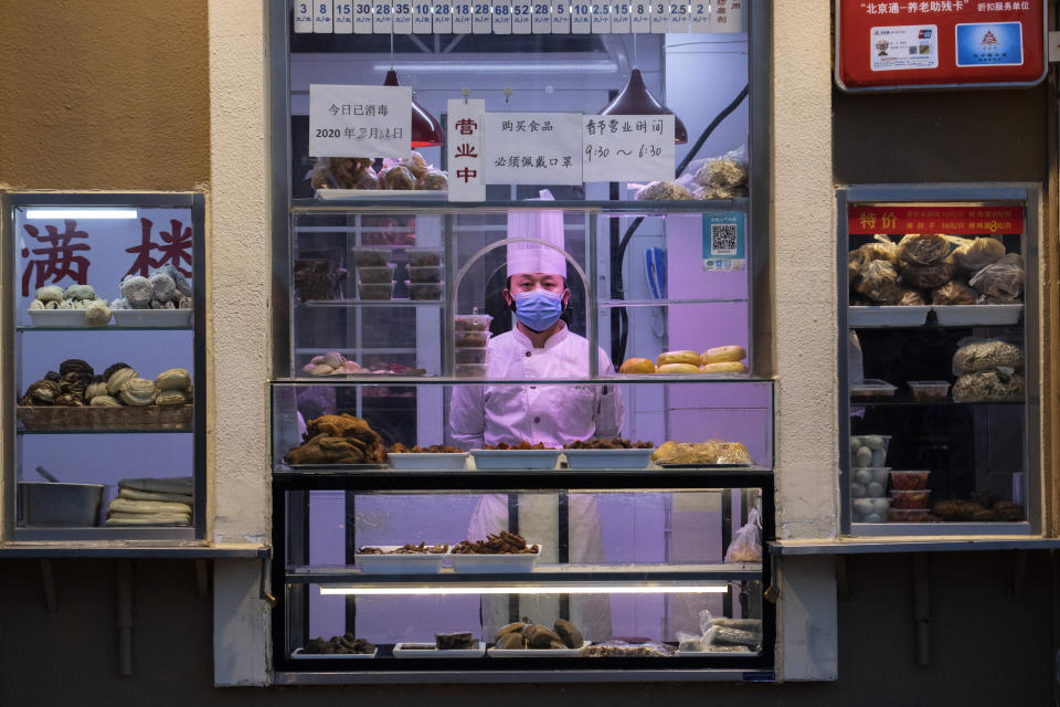 In this photo taken Saturday, Feb. 22, 2020, a chef looks out from behind a display of food products at a restaurant in Beijing, China. Regulators on Monday promised tax cuts and other aid to help companies recover from China's virus outbreak and expressed confidence the ruling Communist Party's growth targets can be achieved despite anti-disease controls that shut down much of the economy. (AP Photo/Ng Han Guan)