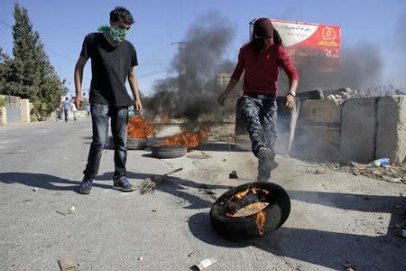 A Palestinian protester kicks a burning tyre during clashes with Israeli troops following the funeral of Palestinian-American youth Orwah Hammad, whom medics said was killed by Israeli forces, in the West Bank village of Silwad near Ramallah October 26, 2014. REUTERS/Ammar Awad