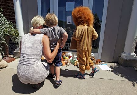 Sarah Madison (L) holds her son Beckett, 3, as her daughter Quinn, 5 (in costume), look at stuffed animals at the doorway of River Bluff Dental clinic in protest against the killing of "Cecil" a famous lion in Zimbabwe, in Bloomington, Minnesota July 29, 2015. REUTERS/Eric Miller