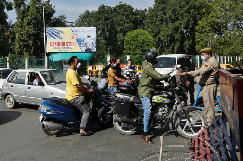 Indian police officers check identification papers of residents at a security barricade during curfew ahead of the first anniversary of the revocation of Kashmir's autonomy, in Srinagar