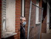 CAPTION CORRECTS THE NAME - In this picture taken Tuesday, May 12, 2020 Iulian, a Romanian worker stands behind the fence that was set up as a quarantine measure at the entrance of a housing of Romanian slaughterhouse workers in Rosendahl, Germany. Hundreds of the workers were tested positive on the coronavirus and were put on quarantine. (AP Photo/Michael Probst)