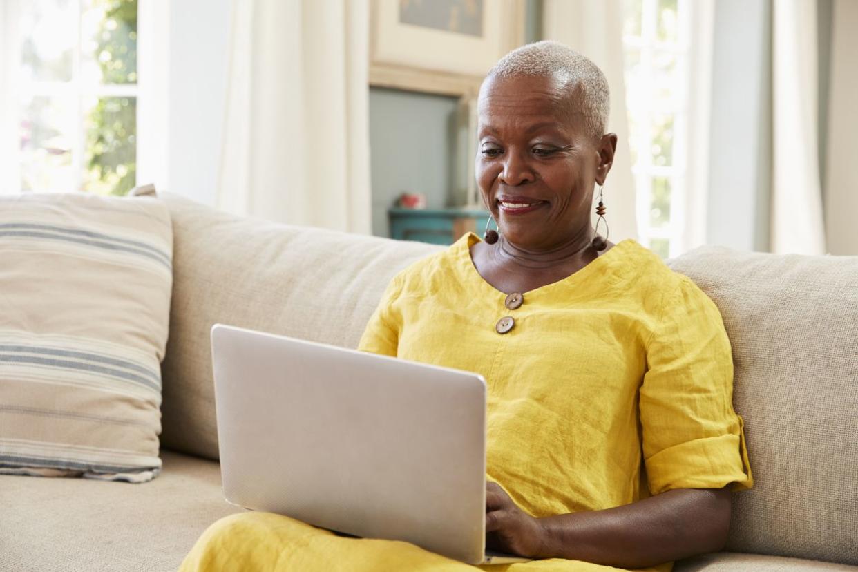 Senior Woman Sitting On Sofa Using Laptop