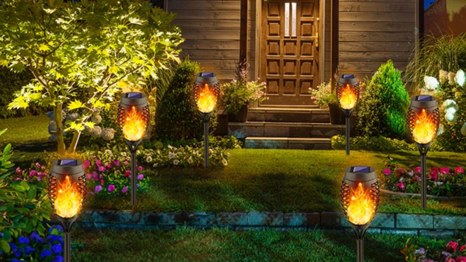 Six solar-powered torches on a lawn leading to the front door of a house. 