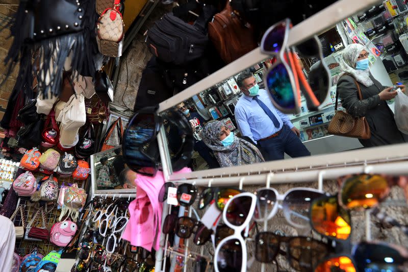 People wearing face masks to help fight the spread of the coronavirus disease (COVID-19) are reflected in a mirror as they walk past a shop displaying its merchandise in Jerusalem's Old City