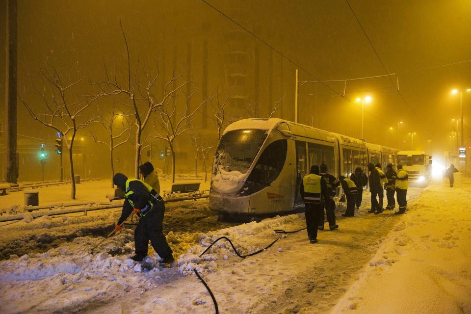 Municipality workers clear snow from the tracks of the light rail tram early morning in Jerusalem