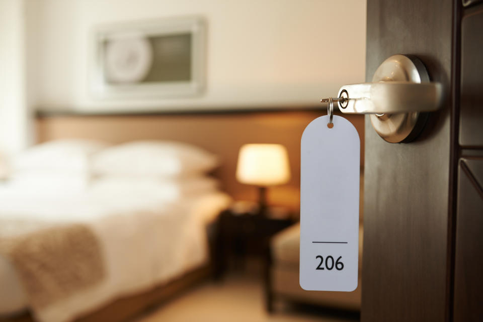 Hotel room door slightly ajar with key and tag labeled "206" hanging from the handle, room interior visible