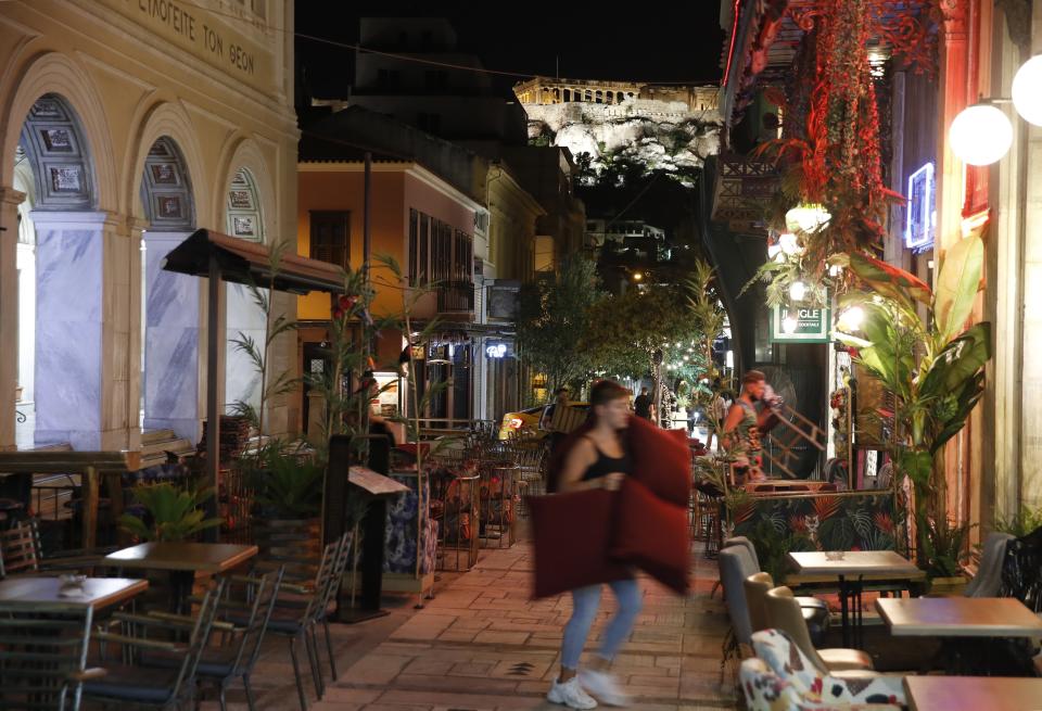 Workers close a bar and a restaurant at midnight, with the Acropolis hill in the background in Athens, Friday, Aug. 21, 2020. Authorities in Greece are using free on-the-spot tests for ferry passengers and nightlife curfews on popular islands to stem a resurgence of the coronavirus after the country managed to dodge the worst of the pandemic. The number of confirmed virus cases and deaths in Greece remains lower than in many other European countries. (AP Photo/Thanassis Stavrakis)