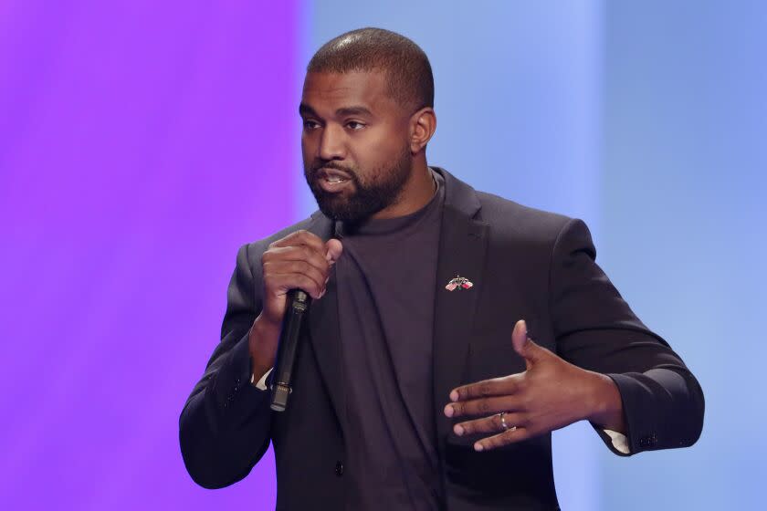 A man in a black suit speaking into a microphone against a purple background