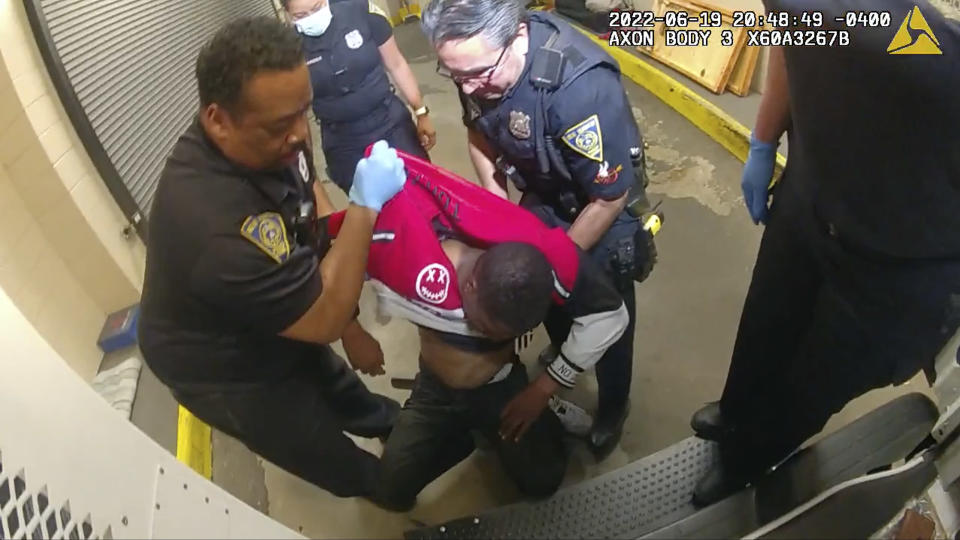 In this frame taken from police body camera video, Richard Cox, center, is placed in a wheel chair after being pulled from the back of a police van after being detained by New Haven Police, June 19, 2022 in New Haven, Conn. Officials in Connecticut said, Wednesday, June 22, 2022, that two New Haven officers have been placed on paid leave and three others were reassigned after Cox was seriously injured in the back of a police van. (New Haven Police via AP)
