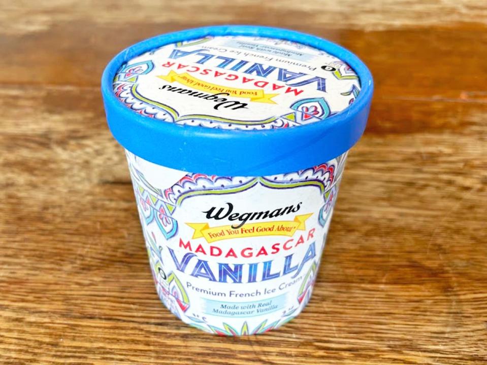 A small pint of ice cream with a blue band around the lid and a design with green, blue, and red detailing. The Wegmans logo is on the front of the ice cream